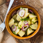 "Close-up view of a vibrant potato salad served in a bowl, featuring diced potatoes, chopped herbs, and creamy dressing, garnished with fresh parsley for a delicious and refreshing look."