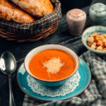 A plate of grilled cheese sandwiches with a steaming bowl of tomato soup.