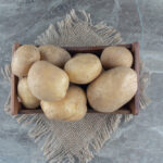 A pile of fresh white potatoes with smooth, light beige skin. The potatoes are irregularly shaped and have a clean, slightly earthy appearance, lying on a plain white surface.