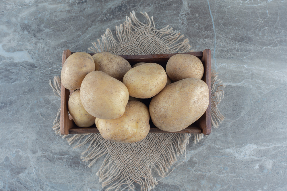 A pile of fresh white potatoes with smooth, light beige skin. The potatoes are irregularly shaped and have a clean, slightly earthy appearance, lying on a plain white surface.